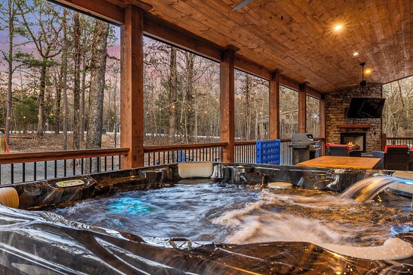 Relax in the hot tub surrounded by a forest view, with a fireplace nearby.