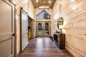 Enter a cozy cabin-style hallway with a polished floor and walls, featuring a large door leading to a room with a fireplace.
