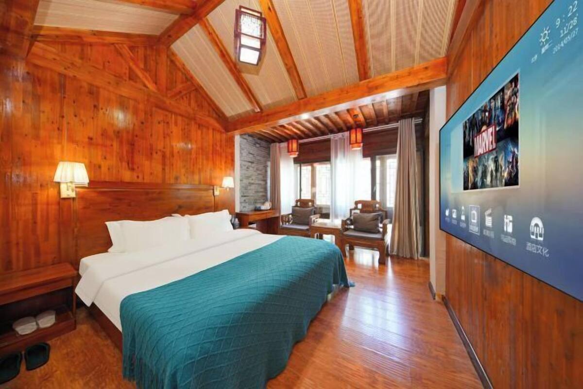 A wooden room with a bed, a desk, and a wall-mounted screen displaying a movie.
