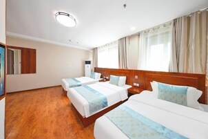 Habitación de hotel con tres camas, suelo de madera, una lámpara en el techo y una ventana con cortinas.