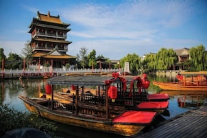 A traditional multi-tiered building with a tiled roof, a wooden boat with red cushions docked in front, and a calm water body reflecting the structure.