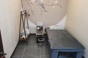 A small room with a bed, a bedside table, a chair, and a wall with a floral mural.
