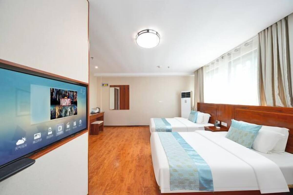A hotel room with two beds, a TV on the wall, a wooden floor, and a window with curtains.