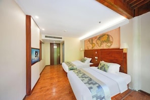 A hotel room with two beds, wooden flooring, a world map on the wall, and a hallway leading to another room.