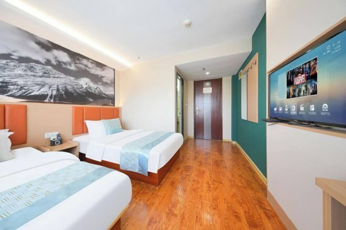 A hotel room with two beds, a flat-screen TV, a painting on the wall, and a wooden floor.