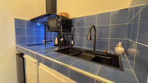 Una cocina con azulejos azules, un lavamanos negro, una cafetera y una campana extractora de acero inoxidable.