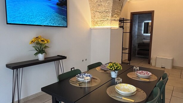 A dining area with a table, chairs, a TV, and a stone wall.