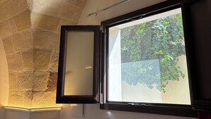 A room with a stone ceiling, a window with a view of greenery, and a red curtain.