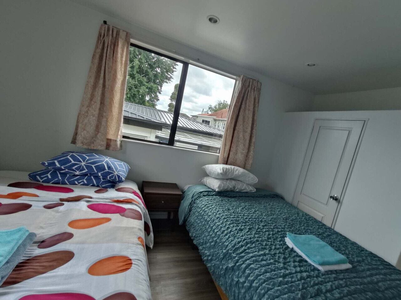 Un dormitorio con dos camas, una ventana con cortinas, una puerta y vistas a edificios.