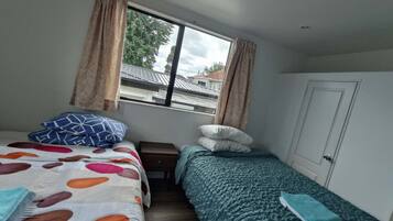 Un dormitorio con dos camas, una ventana con cortinas, una puerta y vistas a edificios.