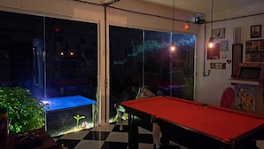 Et biljardbord i et rum med gulv i tern, en glasafskærmning og udsigt ud