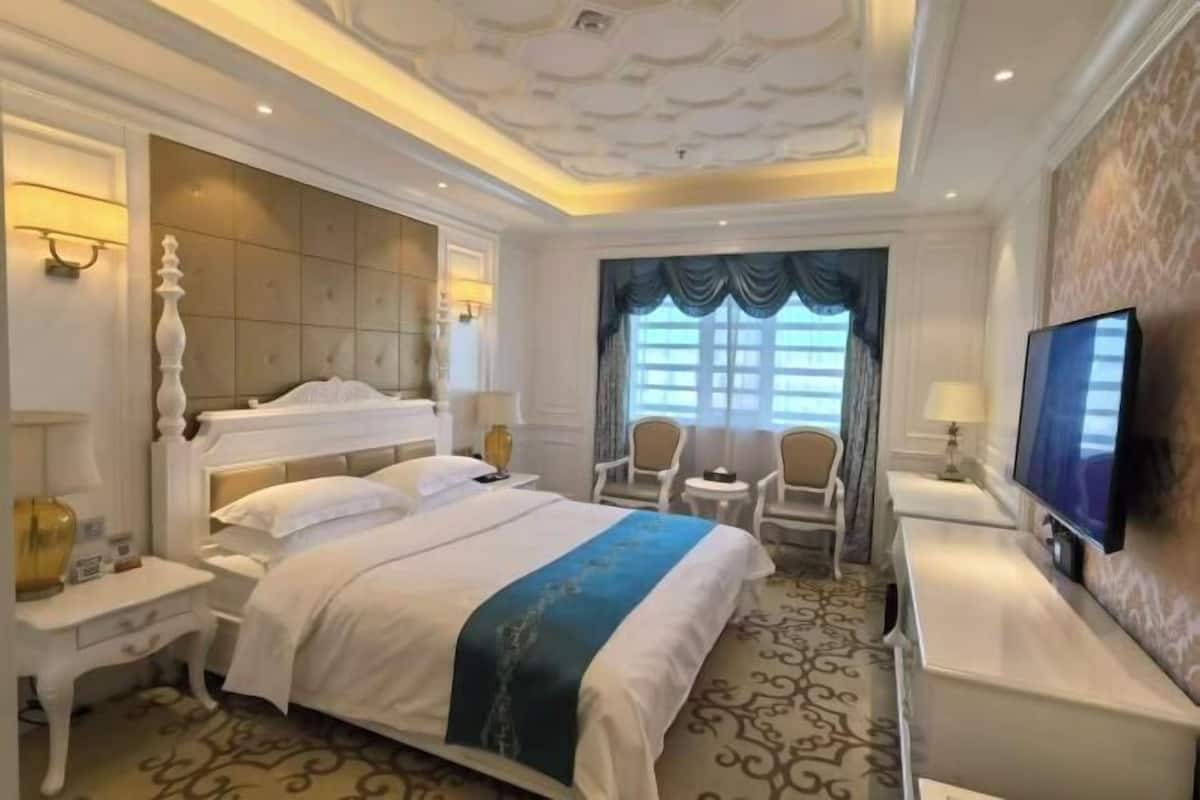 A hotel room with a large bed, a TV, a desk, and a chair.