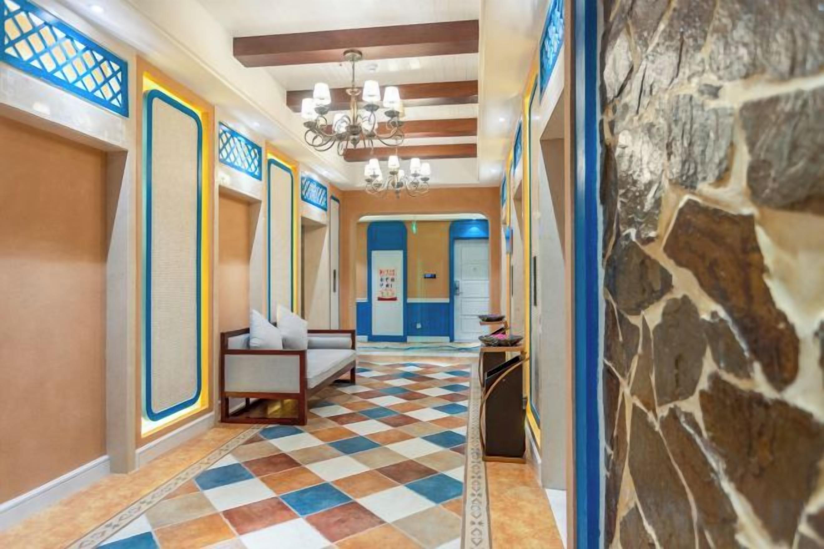 A hotel hallway with checkered flooring, a chandelier, and a stone wall.
