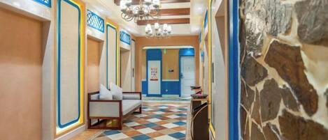 A hotel hallway with checkered flooring, a chandelier, and a stone wall.