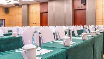 A conference room with rows of tables, each with a green tablecloth, white chairs, and water pitchers.