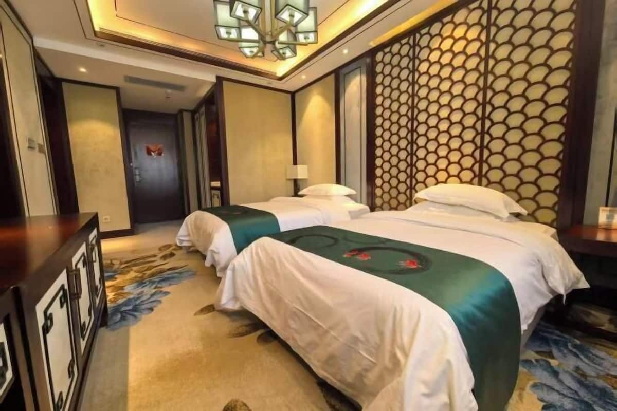 A hotel room with two beds, a decorative wall, and a chandelier.