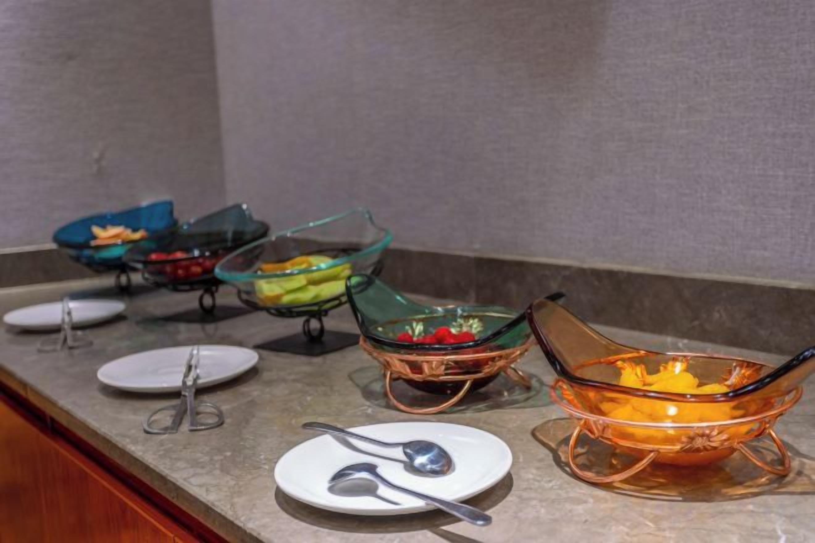 A buffet setup with various glass bowls containing food, accompanied by plates and utensils.