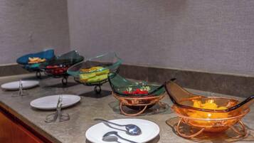 A buffet setup with various glass bowls containing food, accompanied by plates and utensils.