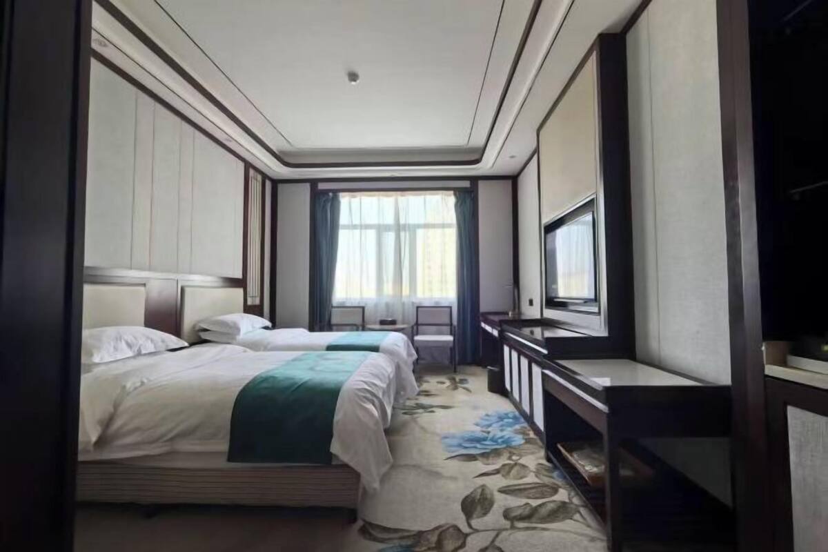 A hotel room with two beds, a television, a desk, and a window with curtains.