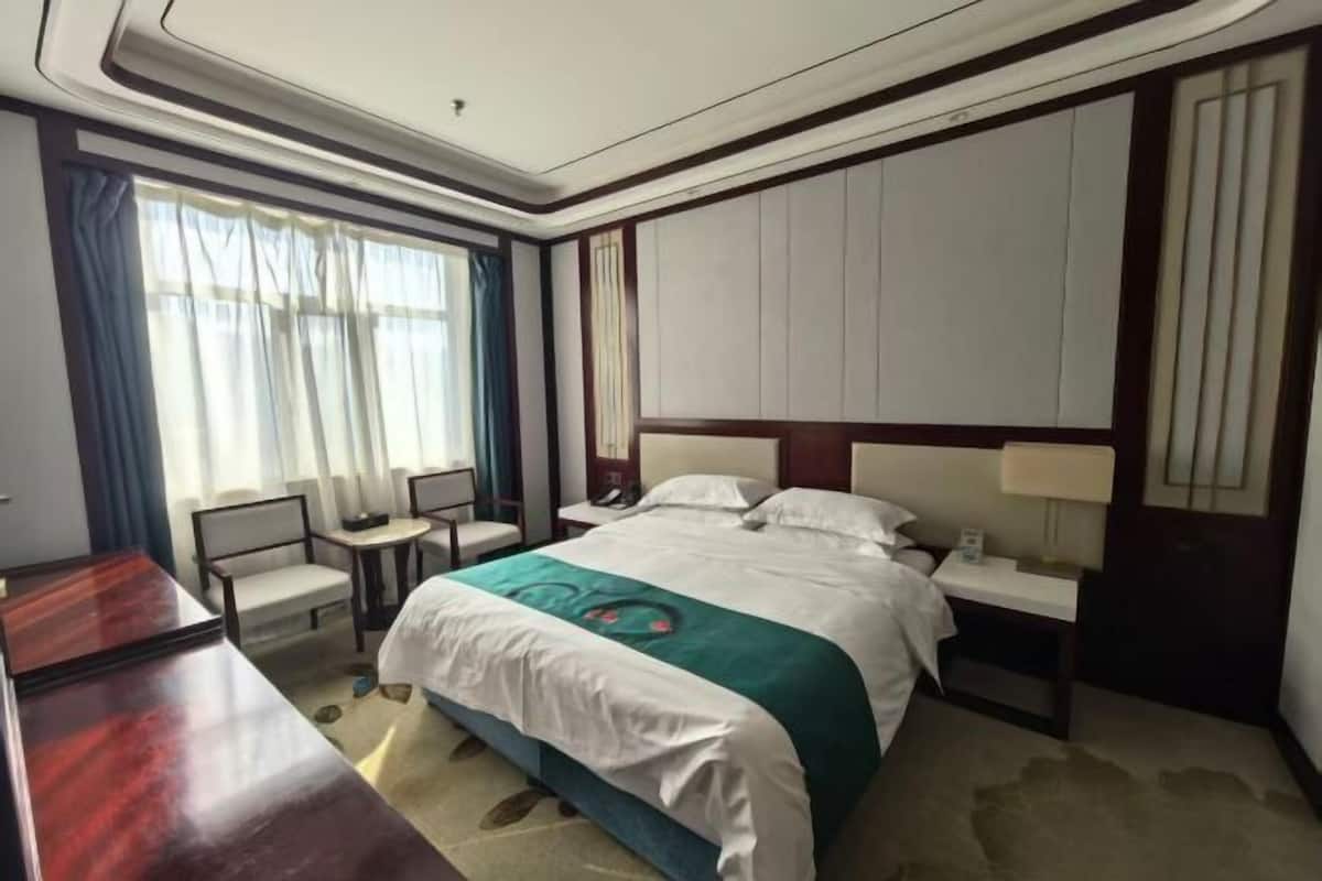 A hotel room with a bed, bedside tables, a desk, and a chair.