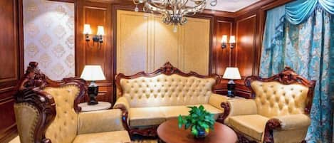 A room with a tufted sofa set, two armchairs, a round coffee table, a chandelier, wall sconces, and patterned wallpaper.