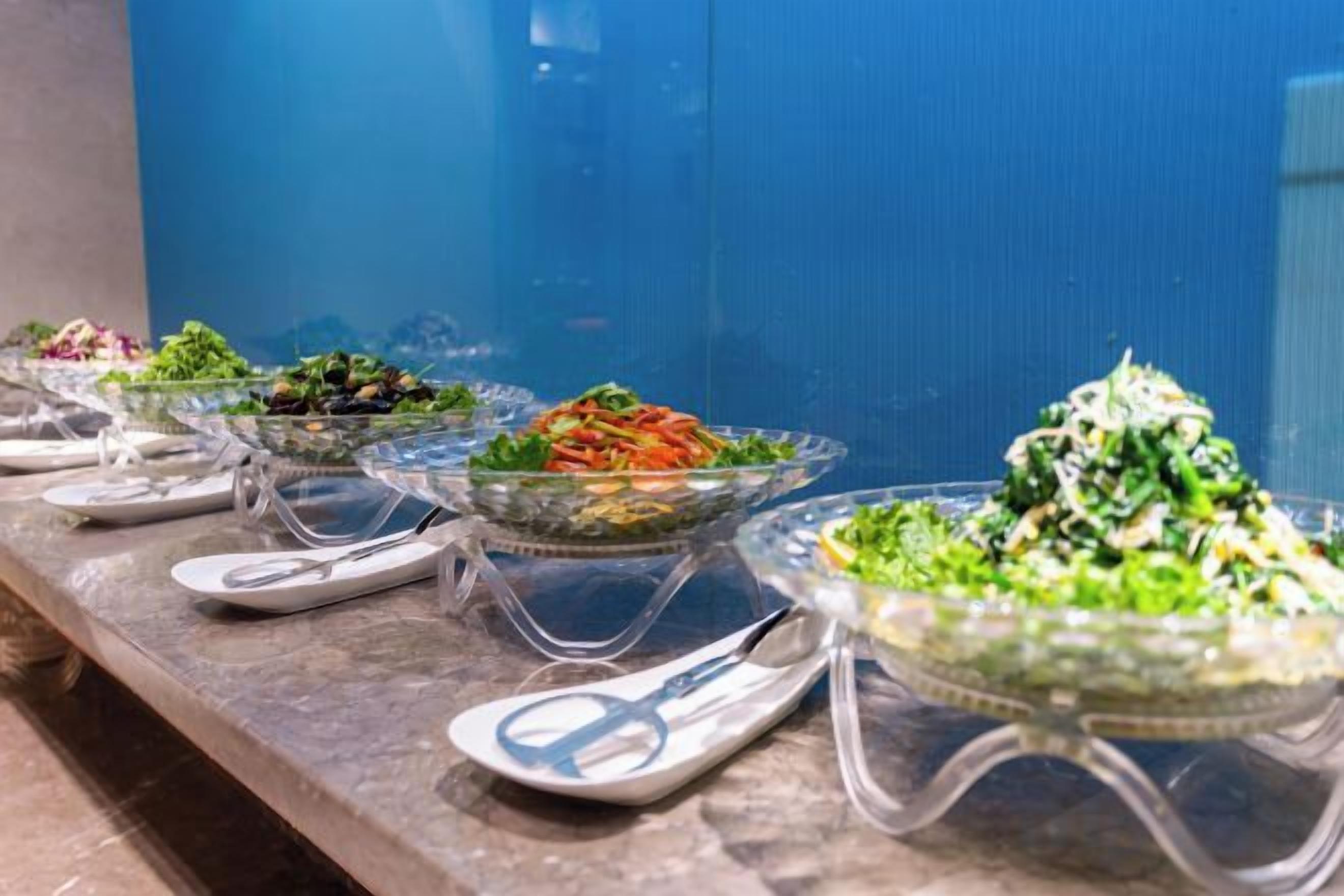 Una mesa de buffet con diversos platos en recipientes de vidrio transparente, dispuestos sobre una encimera de mármol.