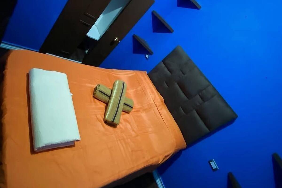 Een bed met een oranje sprei, een wit kussen en een kussen met groene en gele strepen.