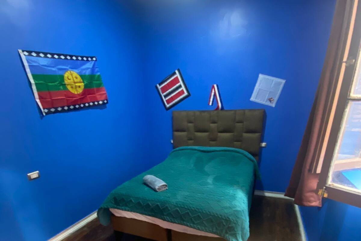 Een kamer met een bed, een tafeltje en een vlag aan de muur.