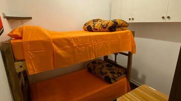 Una cama litera con ropa de cama naranja, un taburete de madera y armarios blancos en una habitación pequeña.