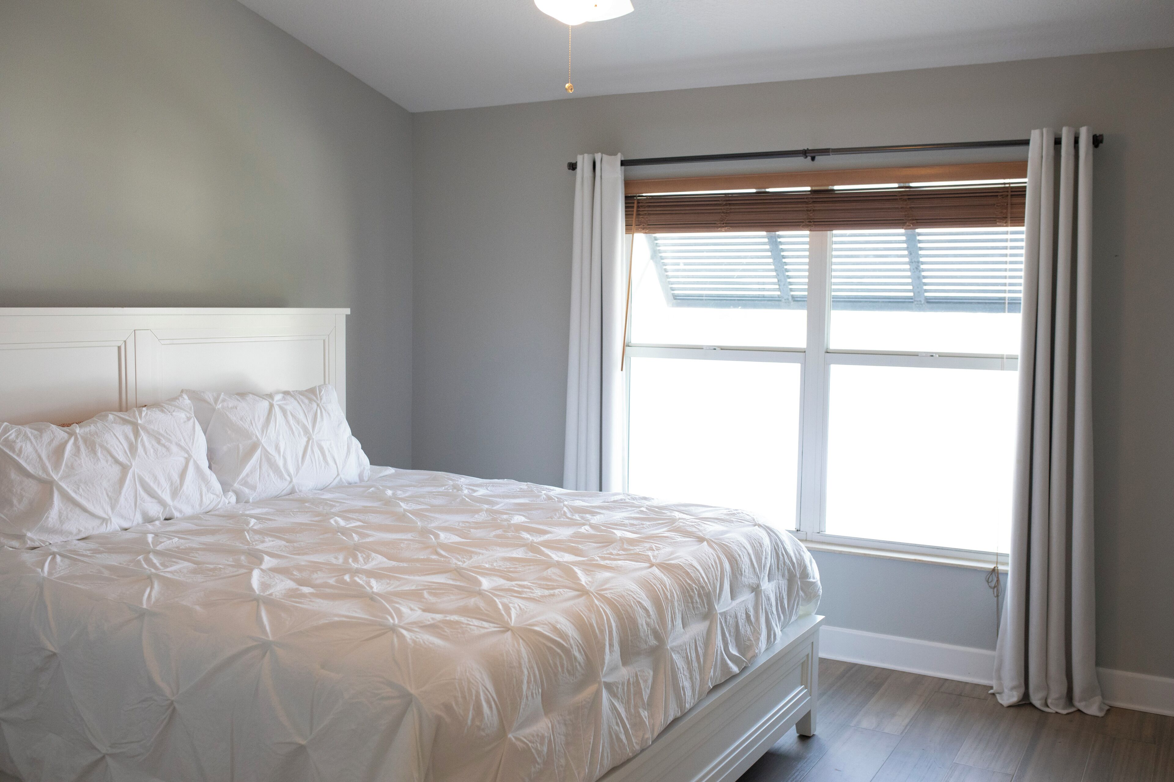 Une chambre avec un grand lit, une fenêtre avec des stores et un luminaire au plafond.