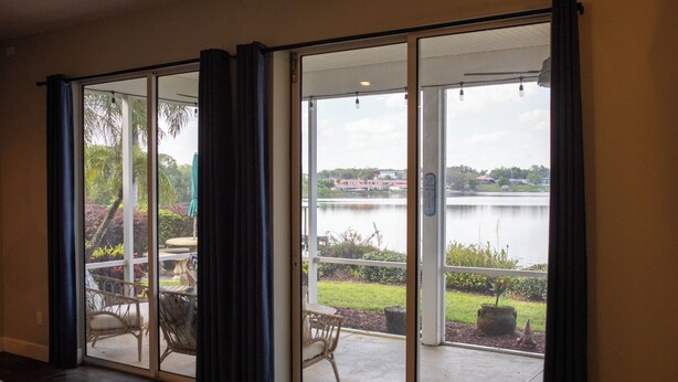 A room with a sliding glass door leading to a patio with outdoor furniture and a view of a lake. - Lakefront Retreat with Pool (Lake Placid)
