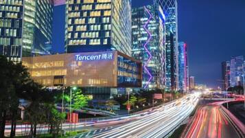 Un paisaje urbano nocturno con edificios iluminados y un destacado edificio de Tencent.
