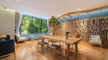 A dining area with a wooden table, chairs, and a view of greenery through large windows.