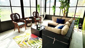 A sunroom with a ceiling fan, wicker furniture, a sofa with cushions, and large windows offering a view of the outdoors.