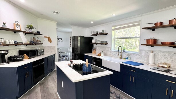 A modern kitchen with dark blue cabinets, a central island, and stainless steel appliances.