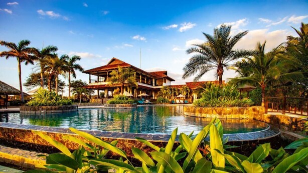 Ein Resort mit großem Pool, Palmen und einem Gebäude mit rotem Dach.