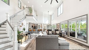 A spacious living area with a gray sectional sofa, a staircase with white railings, and large windows offering a view of greenery. - Lakefront | Dock, 4 Kayaks, Firepit, Sleeps 8 (Lewisburg)