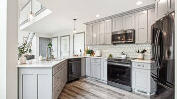 A modern kitchen with grey cabinetry, a stainless steel refrigerator, a built-in oven, and a dishwasher.