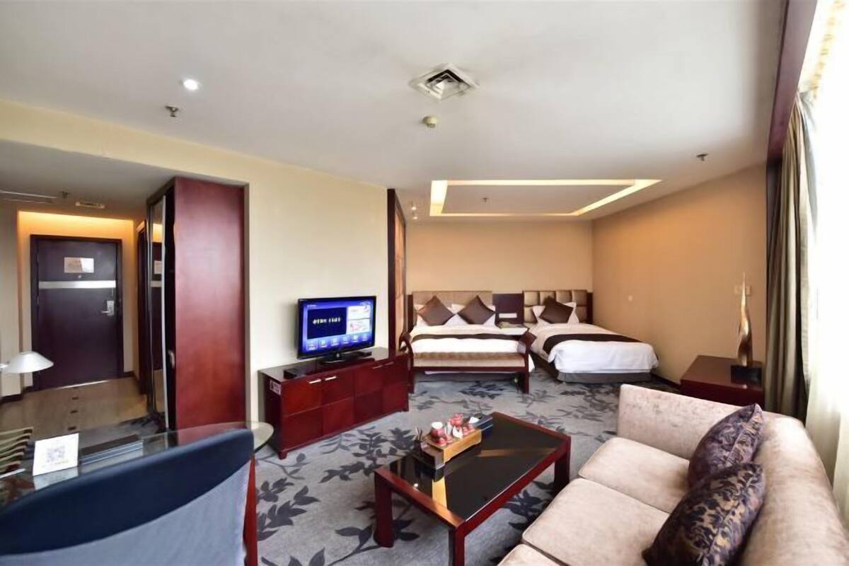 Ein Hotelzimmer mit Bett, einer Couch, einem Fernseher, einem Schreibtisch und einer Rezeption.