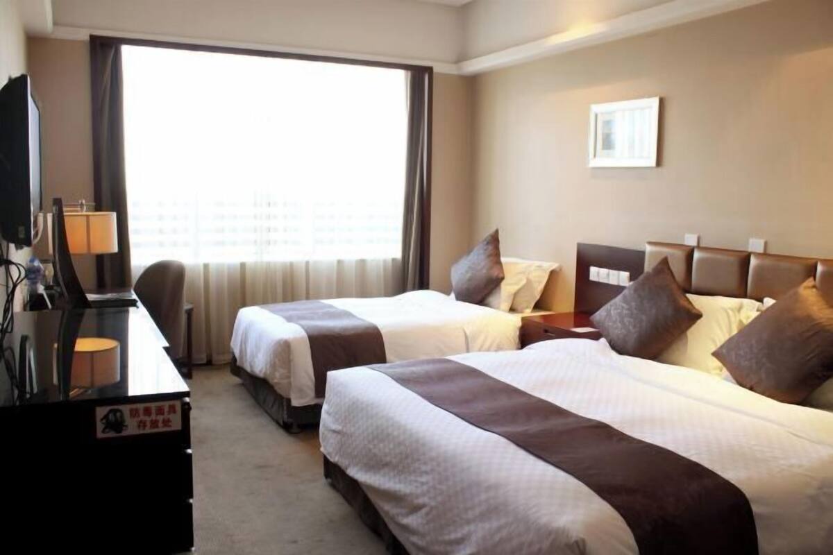 Ein Hotelzimmer mit zwei Betten, einem Schreibtisch mit Lampe, einem Fernseher und einem großen Fenster.
