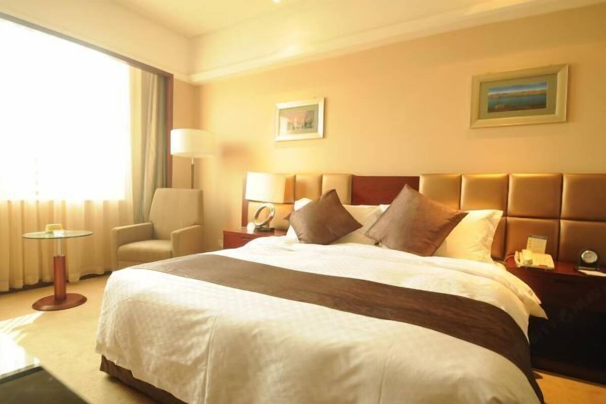 Ein Hotelzimmer mit einem großen Bett, einem Sessel, einem Tisch und einem Fenster mit Vorhängen.