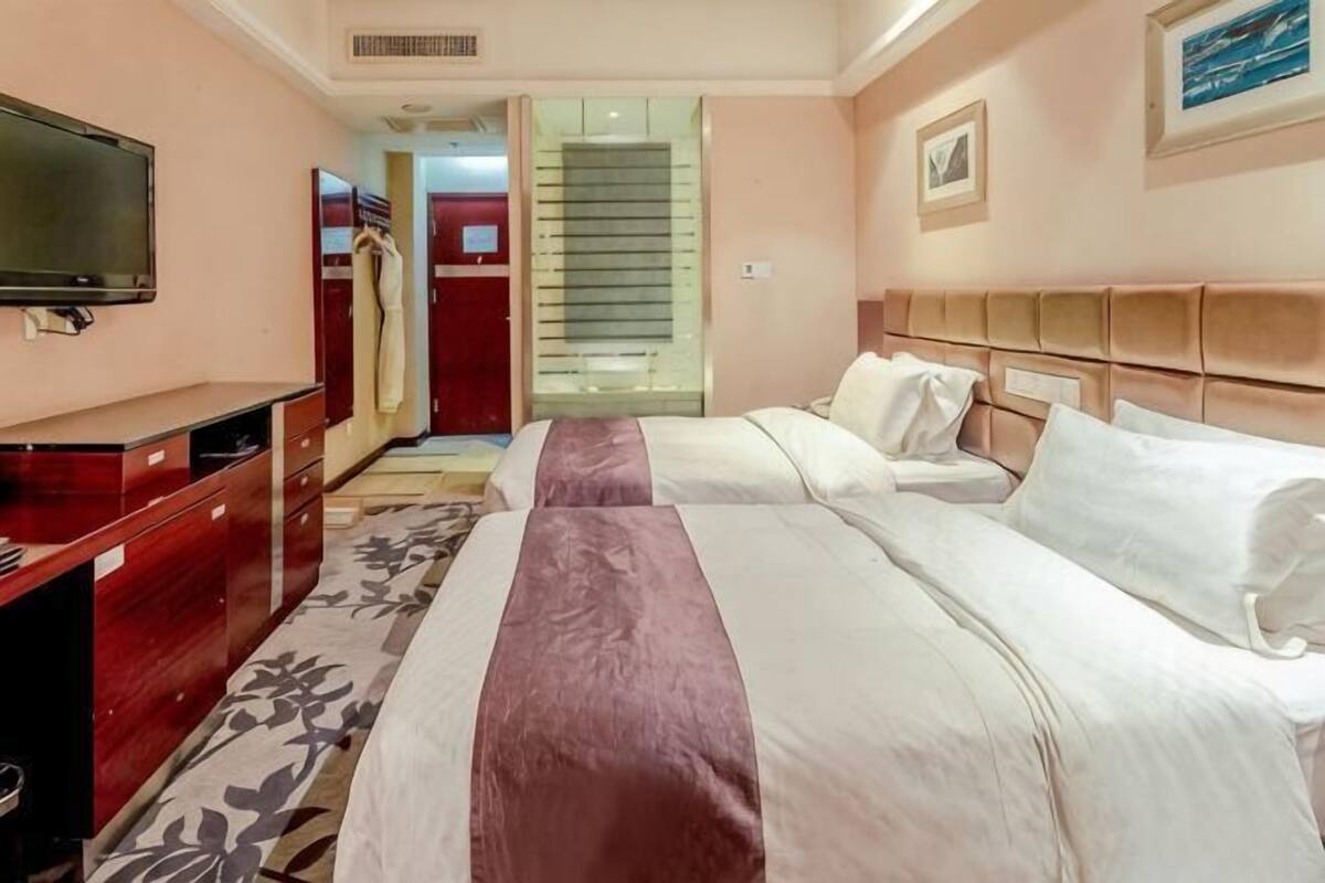 Ein Hotelzimmer mit zwei Betten, einem Fernseher, einem Schreibtisch und einem Kleiderschrank.