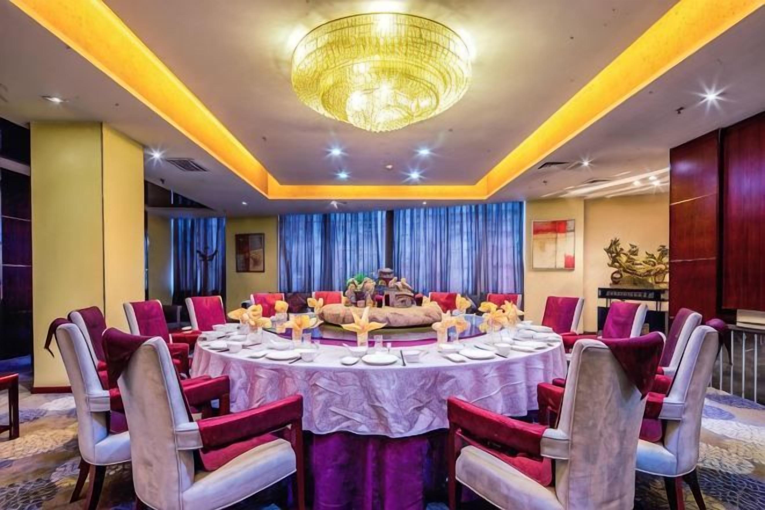 A round dining table with chairs, a chandelier, and a blue curtain backdrop.