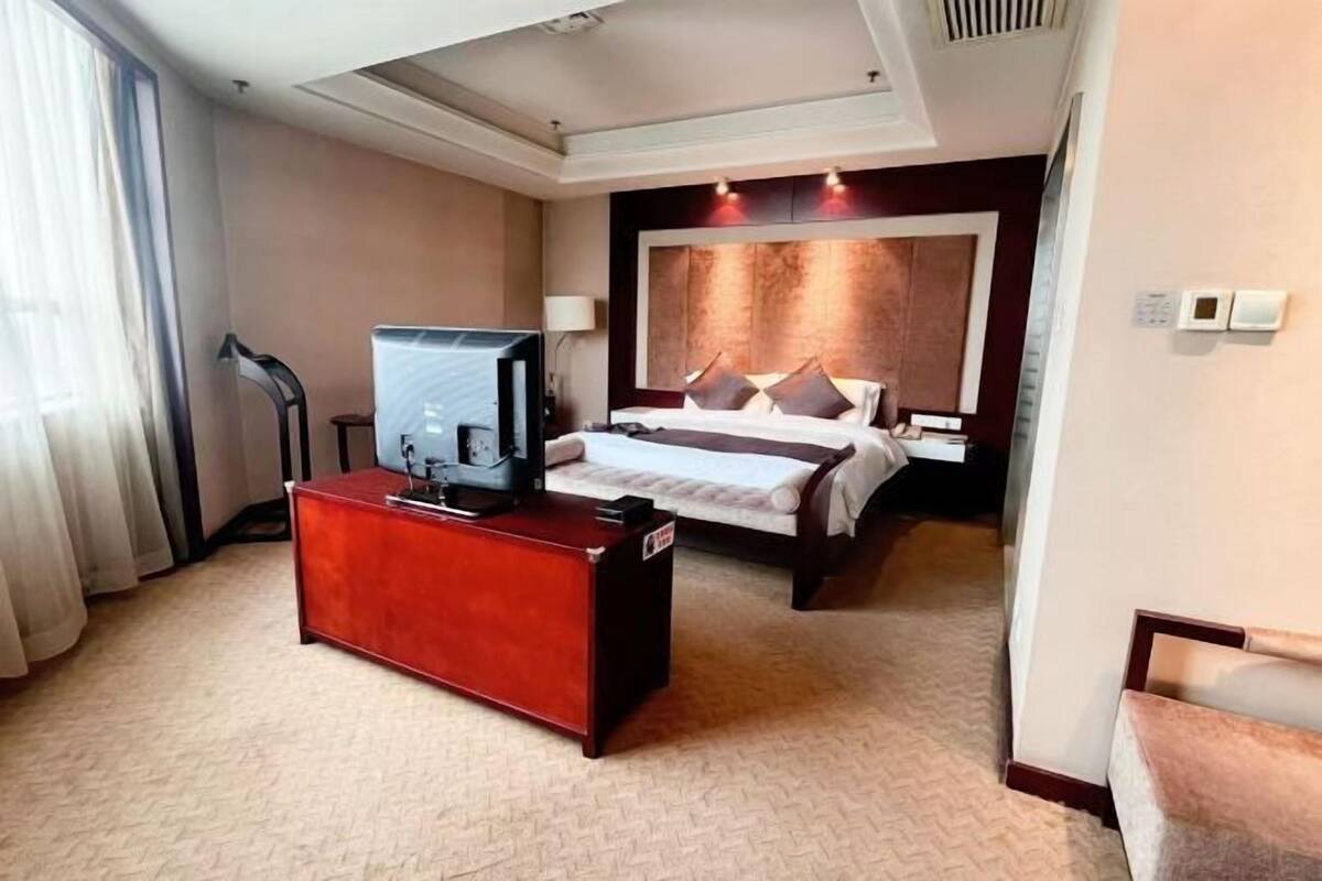 Ein Hotelzimmer mit einem Bett, einem Schreibtisch mit Fernseher und einem großen Fenster mit Vorhängen.