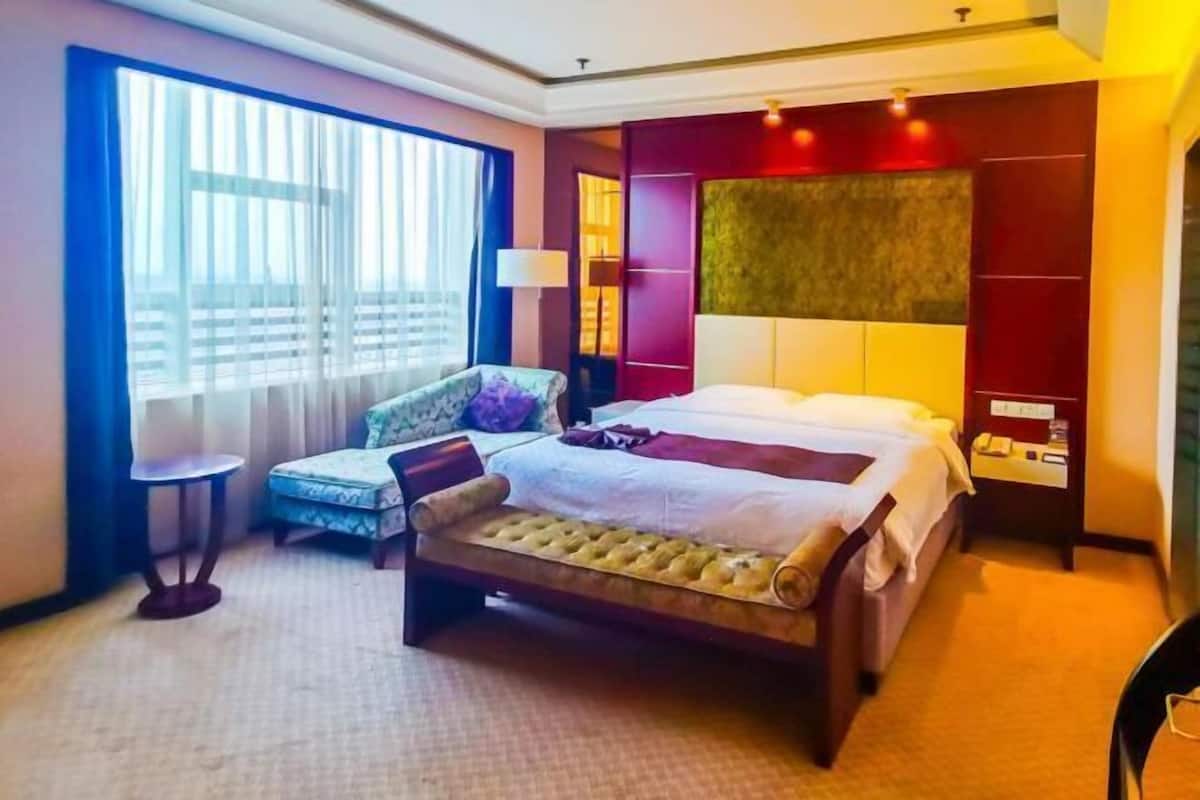 Ein Hotelzimmer mit einem großen Bett, einem kleinen Nachttisch, einem Sessel und einem Fenster mit Vorhängen.