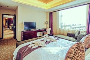 A hotel room with a bed, a TV, a desk, and a window with a view of buildings.
