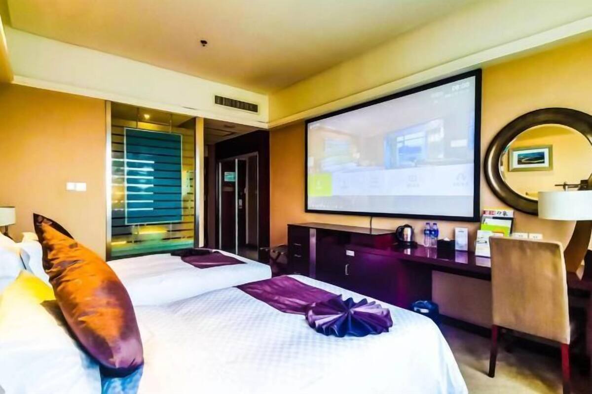 Ein Hotelzimmer mit zwei Betten, einem Schreibtisch, einem Fernseher und einem Spiegel.