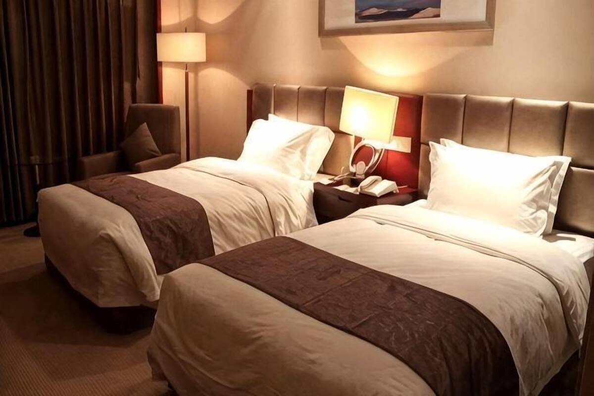 Zwei Betten mit Kopfteilen, ein Nachttisch mit Telefon, ein Sessel und eine Lampe.