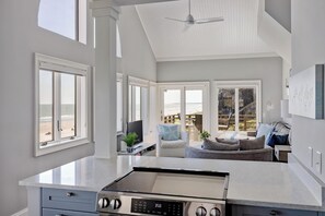 A kitchen with a stove, a dining area with a table and chairs, and large windows with a view of the beach.