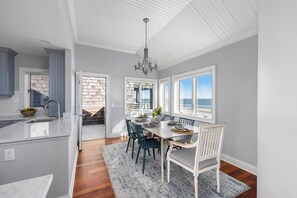 A kitchen with a large island, a dining area with a table and chairs, and a view of the ocean through the windows.
